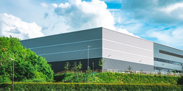 Solar Panels for Warehouse Buildings. An image of the exterior of a warehouse building with surrounding greenery. 